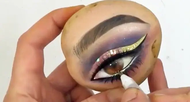 Makeup artist putting makeup on a potato.