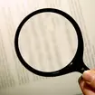 Reading the fine print of a contract/ agreement using a magnifying glass. ASX Au