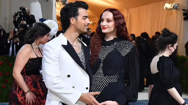 Sophie Turner pregnant and wearing a black dress on the red carpet while Joe Jonas cradles her bump