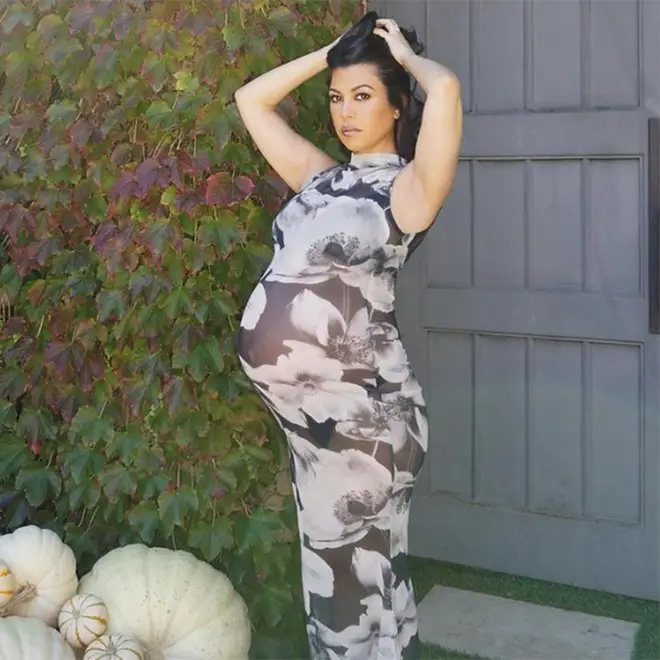 Kourtney Kardashian holding her hair up displaying her baby bump in a sking-tight floral dress